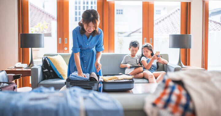 Mother packing luggage at home while two children play in the background