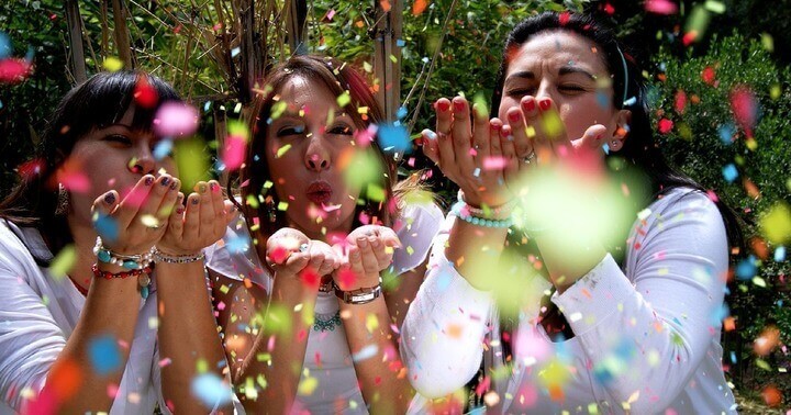 Three women celebrating by blowing on confetti