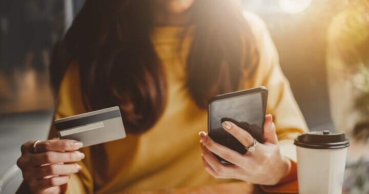 A zoom-in on a woman using her smartphone and credit card to manage her money habits