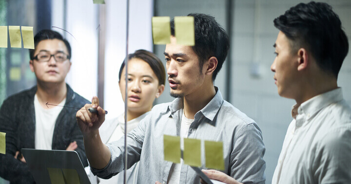 A group of young professional discussing with sticky notes on a glass, judging and perceiving the solutions
