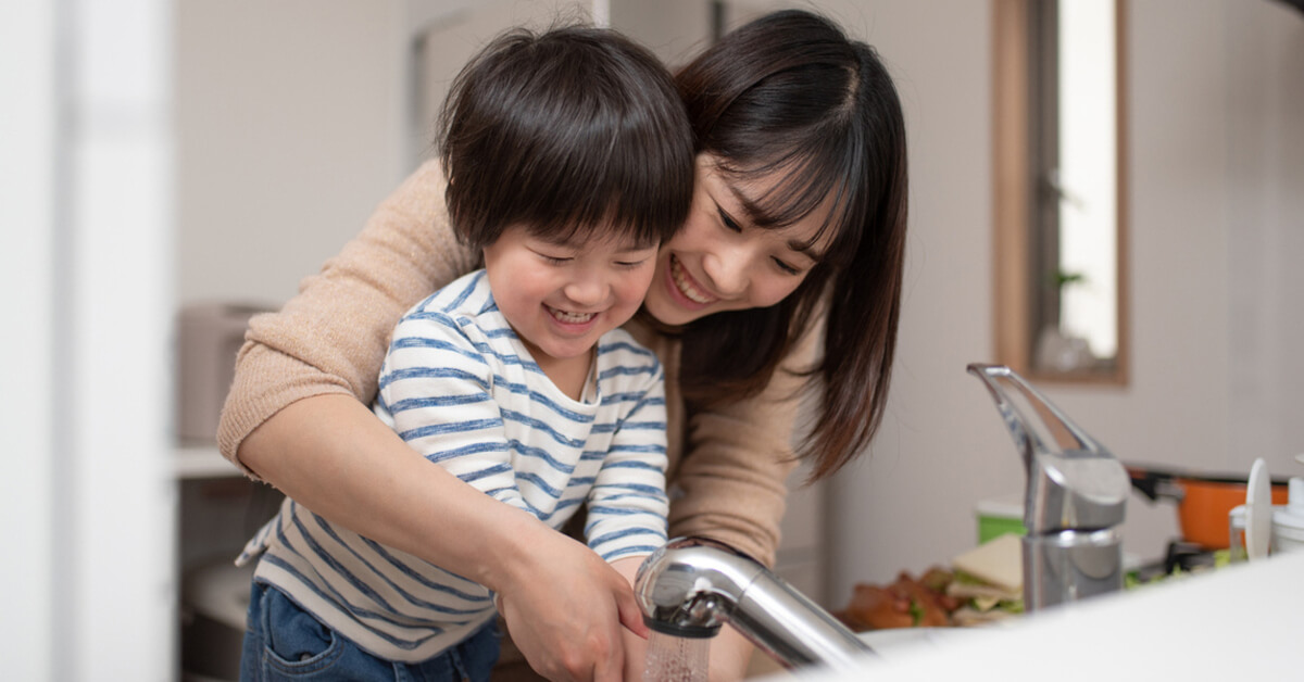 A mother and her child washing hands together at the sink to save water