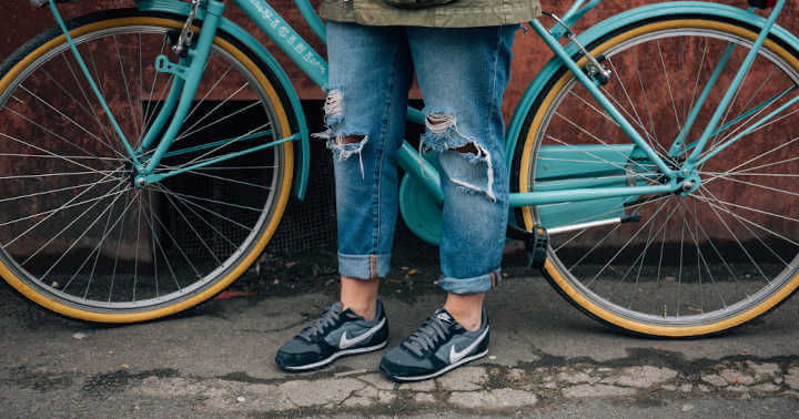 A cyclist in a pair of torn jeans waiting beside a bike with blue rims