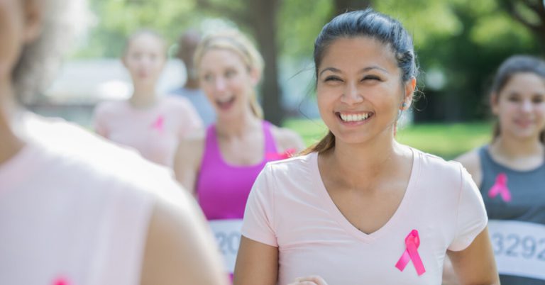 A woman participating in a marathon run for breast cancer awareness with a pink ribbon on her shirt