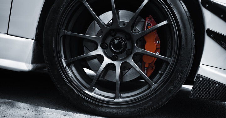 Red coloured break caliper behind the rim of a tyre