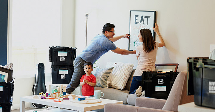 A couple hanging up a picture in the home with a toddler in the living room