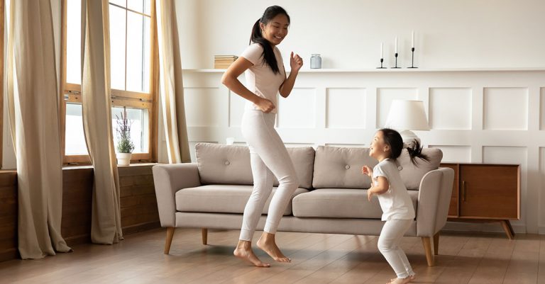 Overjoyed young Asian mom and cute little biracial daughter have fun dancing in living room together, happy millennial mother play involved in funny activity with small Vietnamese girl child at home