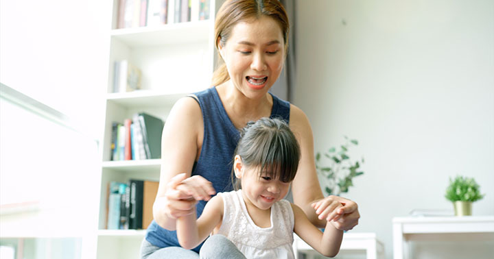 Asian mother and daughter teaching and practicing light yoga exercise on a mat, stretching and controlling the movements on various parts of the body in the brightly lit sunny morning living room
