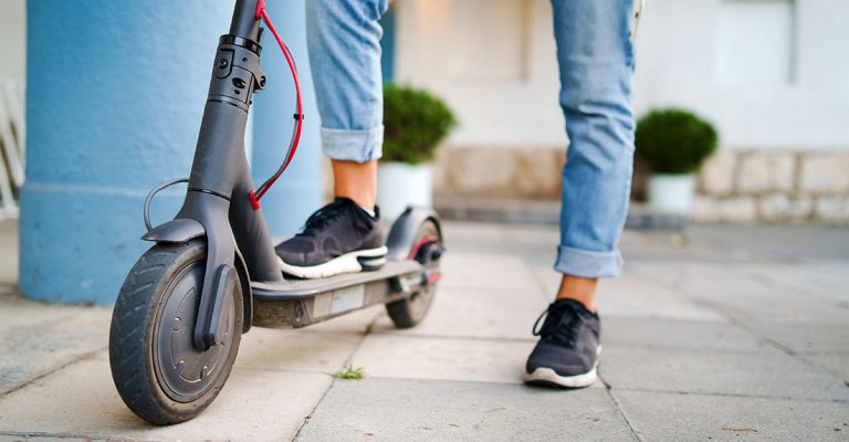 Close up on woman legs feet standing on the electric kick scooter on the pavement wearing jeans and sneakers in summer day