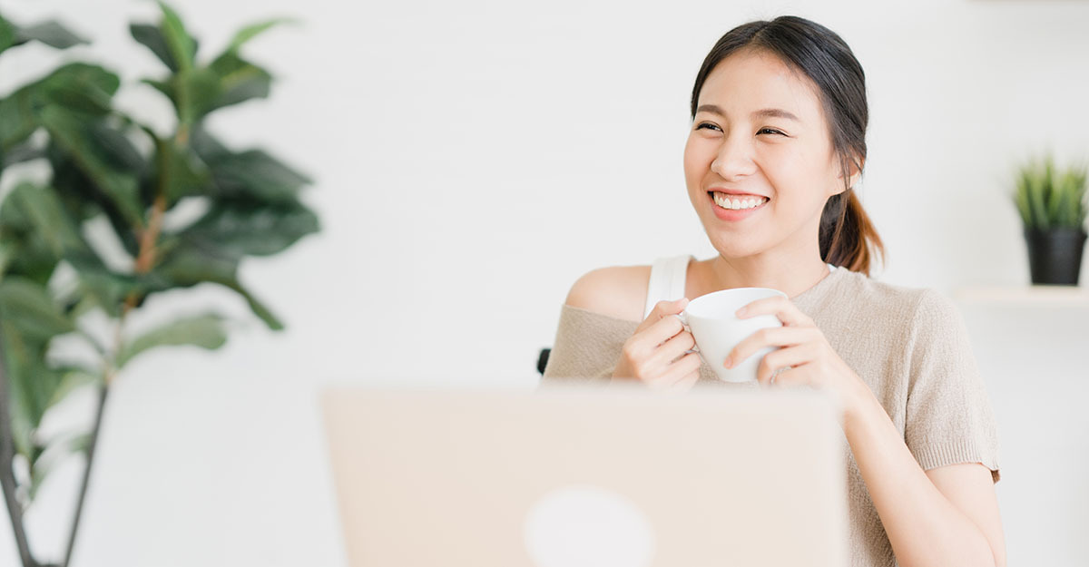 Beautiful young smiling asian woman working on laptop and drinking coffee in living room at home. Asia business woman working document finance and calculator in her home office. Enjoying time at home.