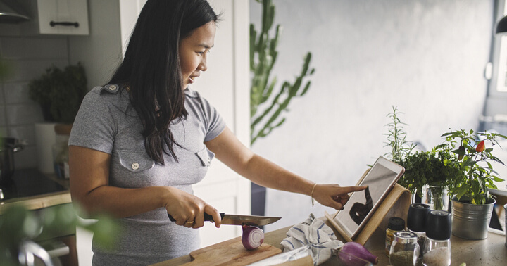 A woman cooking in the kitchen while following instruction on a tablet