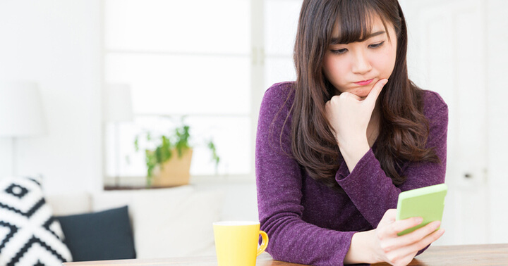 An Asian lady looks at the phone with a contemplative look