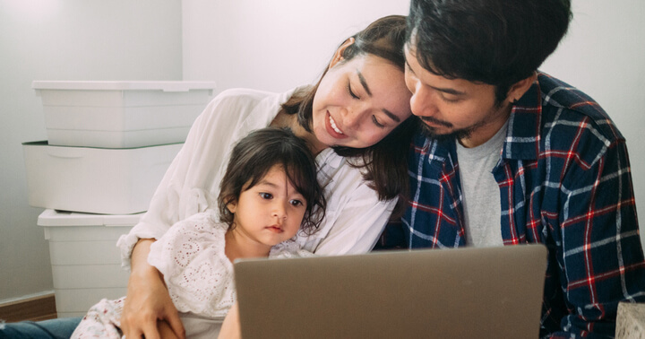 A mother and father looking at their daughter while using the computer together