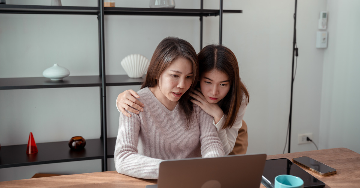 A woman researches about critical illness insurance and death benefits on her laptop in the company of her daughter in their home