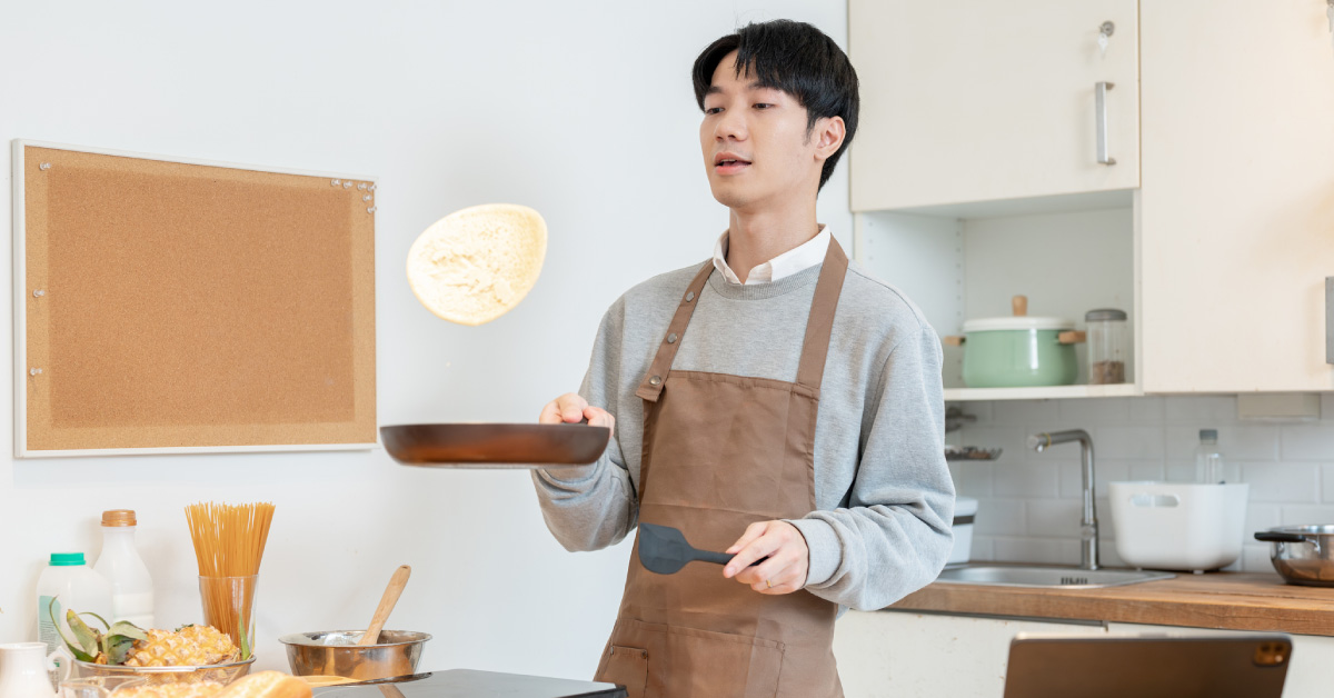 joyful-asian-man-tossing-pancakes-on-a-frying-pan-enjoys-cooking